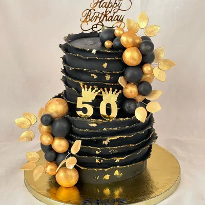Turning 50 in style! This bold black and gold cake makes a glamorous statement with its textured finish, golden orbs, and regal crown details.