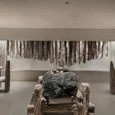 This space in the 'La Solitaire' showroom is a dialogue between stone, wood, and silence. The raw, unfinished textures of the furniture and the massive central stone create a powerful statement of minimalist, nature-inspired design.