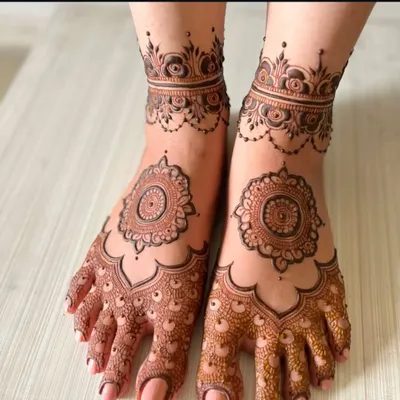 A clean and elegant foot mehndi design. This pattern features a central mandala on the top of the foot with detailed work on the toes and an anklet-style band.