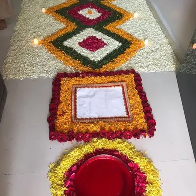 We specialize in detailed floral floor art, known as rangoli. This piece features intricate geometric patterns created with fresh petals of marigold, rose, and jasmine, with small diyas placed to add a warm glow.