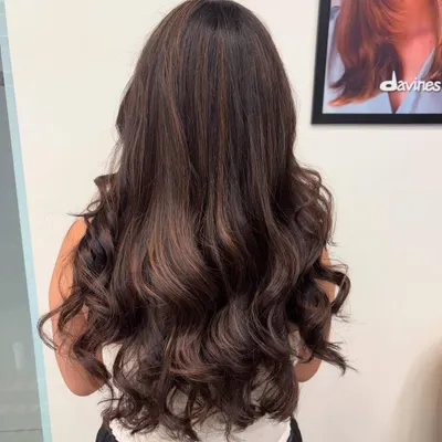 A back view of a rich brunette balayage, styled into voluminous waves. The subtle highlights add depth and movement to the hair.
