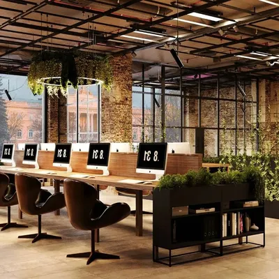 This industrial-style office design uses exposed brick, high ceilings, and abundant natural light to create an inspiring, collaborative workspace. The inclusion of extensive greenery and a central hanging plant feature brings a biophilic element that boosts well-being and creativity.