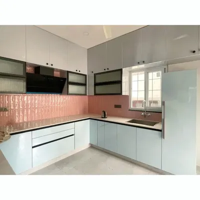 This L-shaped modular kitchen features a unique combination of glossy light blue base cabinets and a striking pink tiled backsplash. The black-framed glass upper cabinets add a modern, industrial touch to this vibrant and functional cooking space.