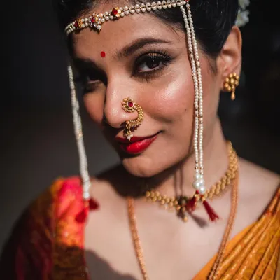 A close-up portrait of a Maharashtrian bride, highlighting her traditional jewelry and confident gaze. The lighting is carefully controlled to create a dramatic, painterly effect.