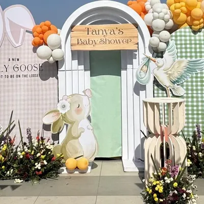 A close-up of the main backdrop for a bunny-themed baby shower. The design features a charming illustration of a bunny and a stork, with a custom wooden sign for 'Tanya's Baby Shower'.