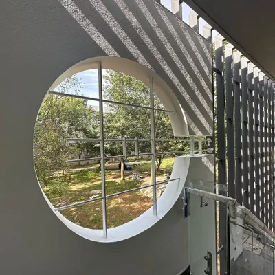 A circular window in the 'Madhuram' project acts as a perfect frame for the landscape outside, while the adjacent slatted screen casts linear shadows.