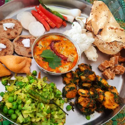 A complete Gujarati thali experience, featuring bajra rotis with vegan butter, dahi tikhari, cabbage and peas sabzi, and more.
