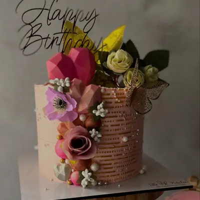 I call this my 'Love Garden' cake. It's a single-tier design with textured pink frosting, adorned with a mix of artificial flowers, geometric hearts, pearls, and a delicate golden butterfly for a whimsical touch.