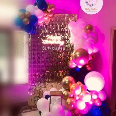 This trendy balloon decoration creates a glamorous photo corner. A gold shimmer wall is framed by an organic balloon garland in shades of blue, white, and gold, perfect for birthdays, bridal showers, or any chic party.