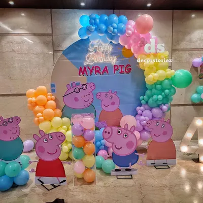 A full view of a Peppa Pig themed birthday party, showcasing multiple character cutouts, a custom backdrop, a light-up number '4', and a colorful pastel balloon arch.