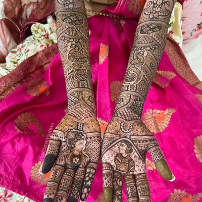 A complete bridal mehendi look featuring portraits of the bride and groom on the palms. The design extends up the forearms with traditional motifs like peacocks and kalash (pots), symbolizing prosperity and love for the new journey ahead.