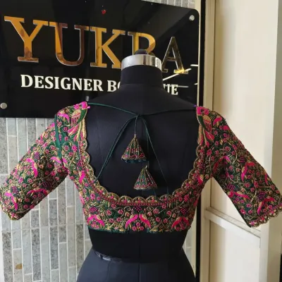 This emerald green blouse features a wide U-shaped back with a beautifully scalloped border. The entire back and sleeves are covered in dense pink and gold floral embroidery, making it a true work of art.
