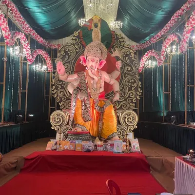 We create magnificent community Ganpati pandals that radiate spiritual energy. This setup features a grand idol on a regal throne, illuminated by a crystal chandelier and framed by elegant green draping and floral arches.