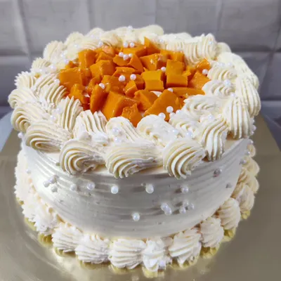 A delicious fresh mango cake. This seasonal favorite is topped with fresh mango chunks and decorated with delicate buttercream piping.
