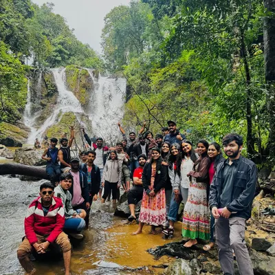 A large, happy group posing in front of a waterfall. This is the community we build every weekend.