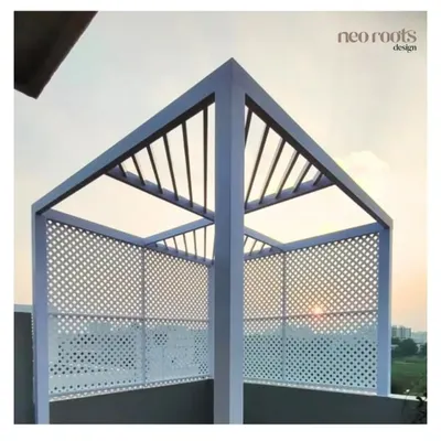 This modern, minimalist pergola on a rooftop features a white metal frame and a slatted roof. The perforated side panels offer partial privacy while creating beautiful light and shadow patterns, perfect for enjoying a sunset view.