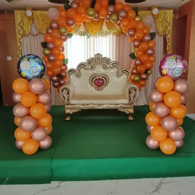 A traditional baby shower stage setup with an orange balloon arch and a decorative sofa for the mother-to-be.