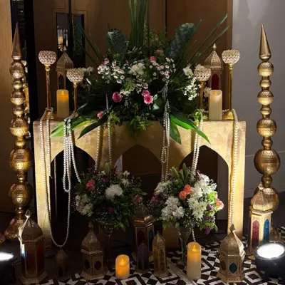 An opulent decor corner for a 10th-anniversary party. This setup features Moroccan-style lanterns, pearl strings, and floral arrangements on a carved table, creating a rich and romantic atmosphere.