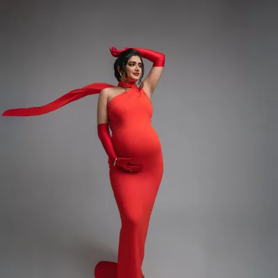 Owning the moment in a striking red halter gown. This look is all about celebrating your confidence and power, with a flowing scarf that adds a touch of dynamic elegance to this fashion-forward maternity portrait.