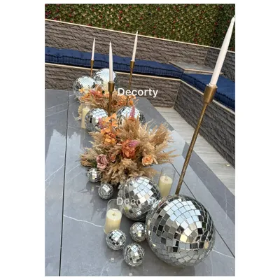 An ultra-chic table centerpiece for a 'Disco Night' adult birthday party. The runner is made of disco balls of various sizes, dried pampas grass, and tall, elegant candle holders.