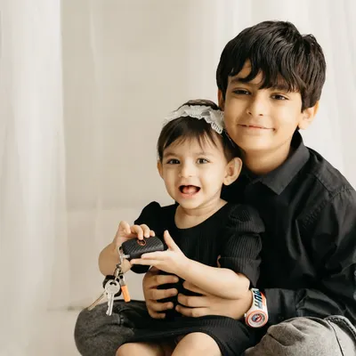 An older brother holds his baby sister, who is happily playing with a set of keys. A real, candid sibling moment.