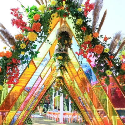 A stunning triangular entrance tunnel made of colorful glass panels and flowers. This 'Glistening Glass' Haldi theme was all about modern design and vibrant colors.
