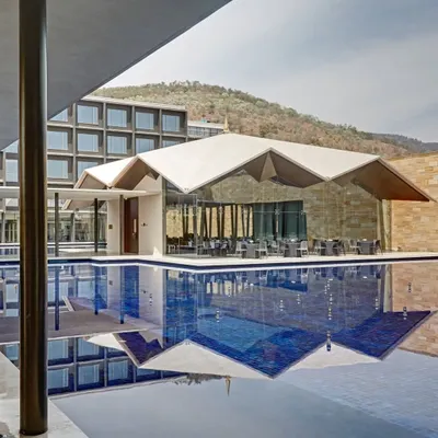 The Lotus Cafe seen from across the pool, its geometric roof reflected perfectly in the water, creating a striking modern landmark against the backdrop of the Tirumala hills.