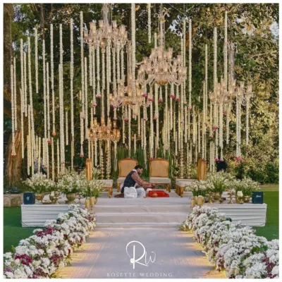 This stunning outdoor mandap is the epitome of an enchanted garden wedding. Crystal chandeliers and strings of white flowers hang from the trees, creating a magical canopy above the couple for a truly soulful ceremony.