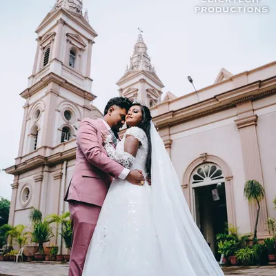 A beautiful wide-angle shot of a Christian bride and groom embracing in front of the church, with the bride's long veil adding a touch of elegance to the portrait.