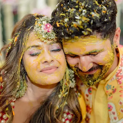 An intimate moment amidst the joyous chaos of the Haldi ceremony. The couple finds a quiet second together, covered in turmeric and love.