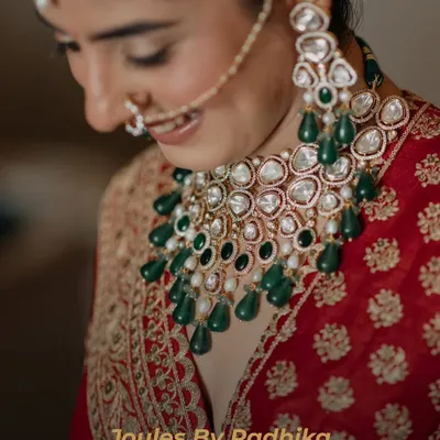 Not just a bride, but a vision. This close-up captures the radiant smile of a JBR Bride, adorned in a bespoke polki necklace with cascading emerald drops, perfectly complementing her red bridal attire.