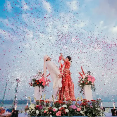 A sundowner varmala by the lake is pure magic. This wide shot captures the stunning sky, the flower shower, and the couple's joy, creating a breathtaking image.