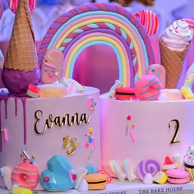 This "Too Sweet" themed double birthday cake was a joy to create for a second birthday party. It features two separate cakes connected by a fondant rainbow and decorated with macarons, lollipops, and ice cream cones for a truly magical look.