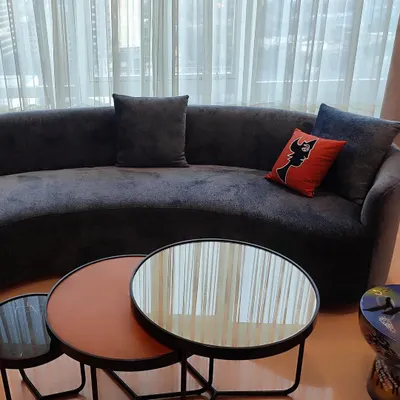 This curved sofa, upholstered in a deep charcoal velvet, anchors the room with presence and understated grandeur. The fabric's soft sheen catches the light, highlighting its sculptural form and creating a sophisticated focal point.