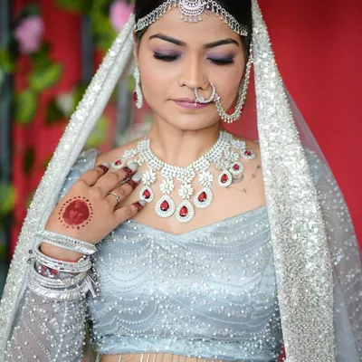 A close-up of a bridal look where the nails are a key accessory. The classic red gel polish on these custom extensions was chosen to perfectly match the ruby details in her necklace and her light blue lehenga.