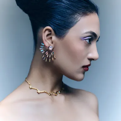 A profile shot from a jewelry editorial, providing a clear view of these stunning fan-shaped earrings and a delicate gold necklace. The model's elegant updo and clean makeup ensure the jewelry remains the focal point.