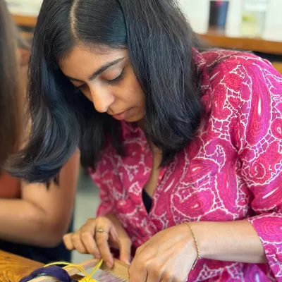 A participant finding her creative flow during a frame loom weaving session. You can see the focus and care she puts into her mini tapestry as she works with colorful yarns, learning different handweaving techniques and patterns.