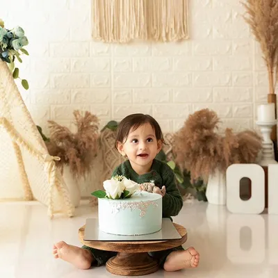 A baby boy sits with his first birthday cake during a boho-themed cake smash session, ready to dig in.
