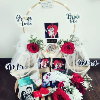 This engagement hamper is designed to celebrate a new beginning. It features a custom ring-shaped platter decorated with fresh flowers, personalized photos of the couple, and fun "Bride to be" and "Groom to be" signs, making it a perfect gift to mark the special occasion.