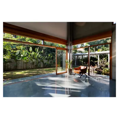 An empty room in the 'House of Canopies' project, where the polished concrete floor reflects the garden outside. The floor-to-ceiling glass doors open completely, transforming the living area into a covered pavilion within the landscape.