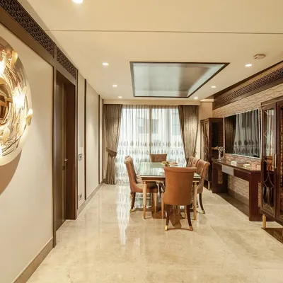 A classic dining setting where warm walnut furniture is set against beige walls and polished marble floors. The space is elevated by a sculptural gold wall mirror and custom display cabinets, creating an environment of quiet sophistication.