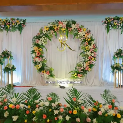 A beautiful and classic engagement decor. The large floral ring with the couple's initials, set against a simple white drape, creates an elegant and personalized stage.