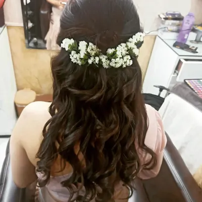 This half-up, half-down hairstyle features voluminous curls and a crown of fresh baby's breath flowers. It's a romantic and popular choice for engagement and mehndi ceremonies.
