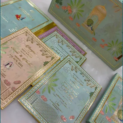 A stunning wedding invitation suite featuring a pastel green box with a peacock motif. The set includes multiple inserts for different events, all coordinated with gold foil detailing for a touch of royalty.