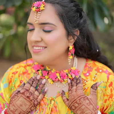 A close-up of the radiant Haldi bride. The soft pink eyeshadow and dewy skin create an ethereal glow, perfectly complemented by her intricate henna and floral jewellery.