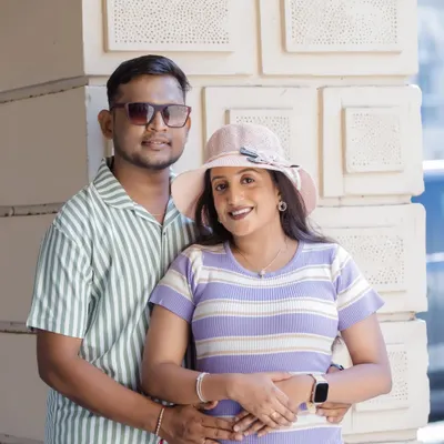 A relaxed and happy couple posing for a maternity portrait against a modern, textured wall. Their casual, coordinated outfits and easy smiles make this a perfect example of a contemporary and informal pregnancy photoshoot.