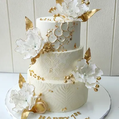 A golden celebration for a golden milestone. This elegant three-tier anniversary cake features intricate textures, delicate white sugar flowers, and luxurious gold accents, designed to reflect timeless beauty and sophistication.