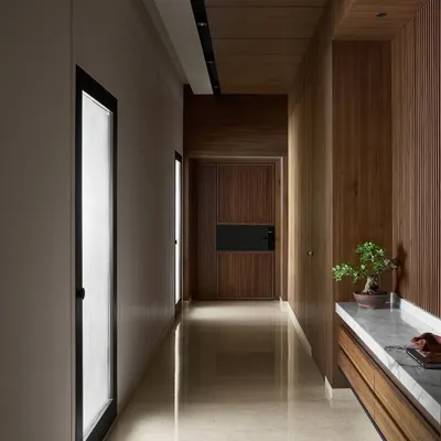 The entrance to Lumen House sets a warm, inviting tone with fluted wood panels and a polished marble floor. The passageway is designed to create a sense of transition, leading the eye towards the bright, open-plan living area.