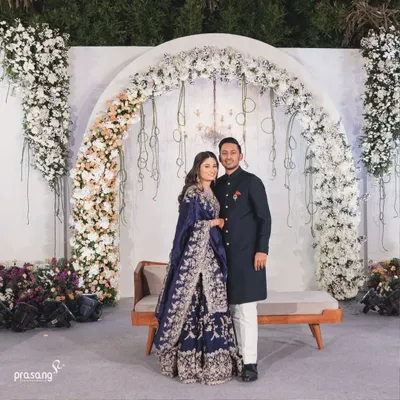 A picture of elegance. The couple stands before a beautiful floral arch of white roses, a classic and timeless backdrop for a reception. My designs focus on creating sophisticated settings for your most important photos.