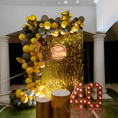 A glamorous 40th birthday celebration with a gold and black theme. This setup features a gold shimmer wall, a balloon half-arch, and large marquee numbers for the age.